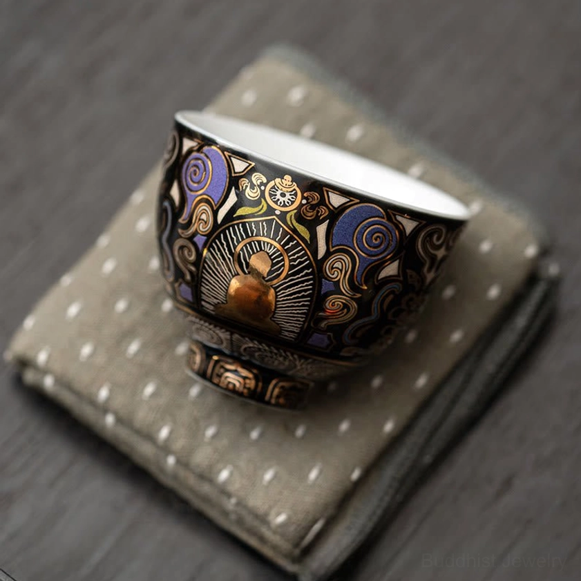 Overhead view of black Thangka Buddhist ceramic tea cup resting on decorative linen coaster, showing unified decorative style