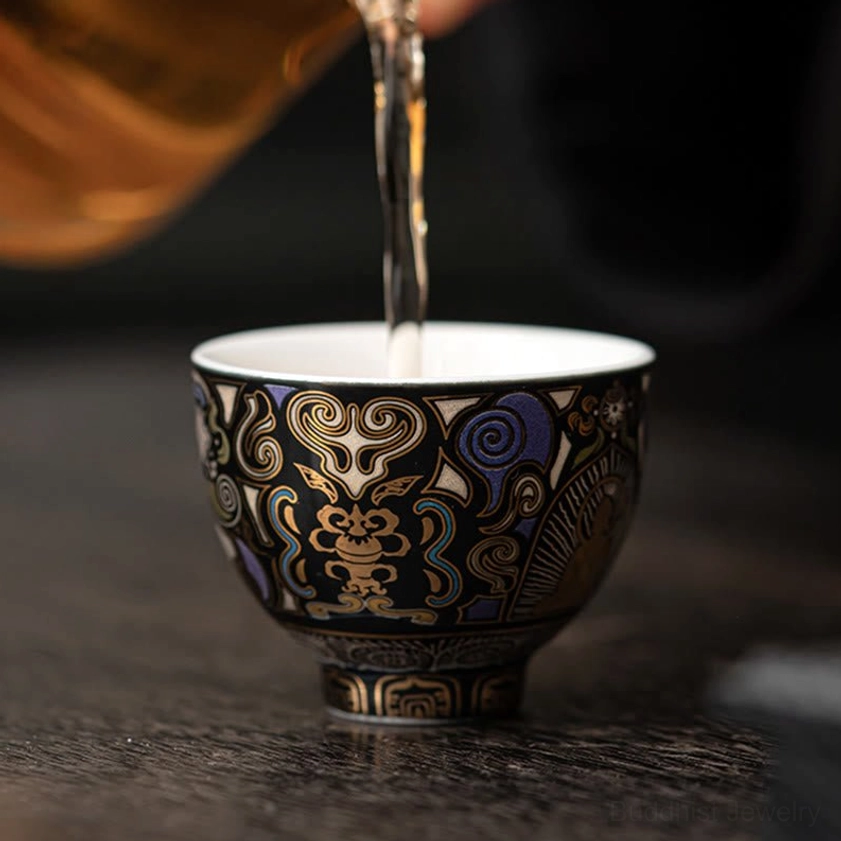 Hot tea being poured into black Thangka Buddhist ceramic cup on dark wooden tea table, demonstrating mindful tea ceremony ritual