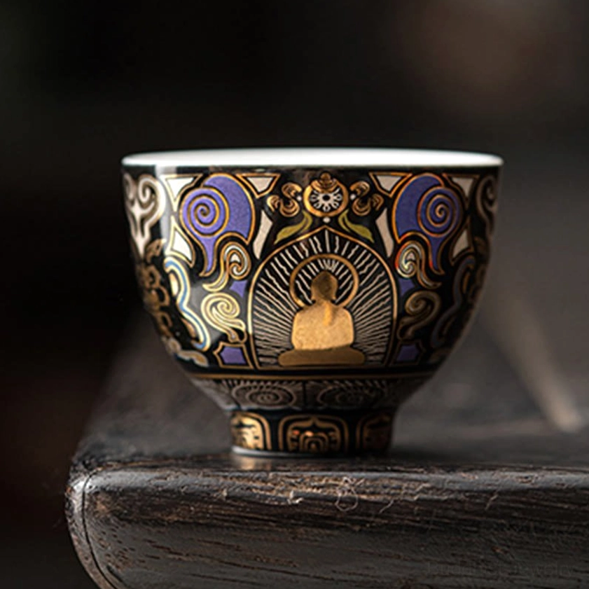 Thangka Buddhist tea cup with gilded Buddha silhouette and decorative auspicious cloud patterns displayed on dark wooden tea table