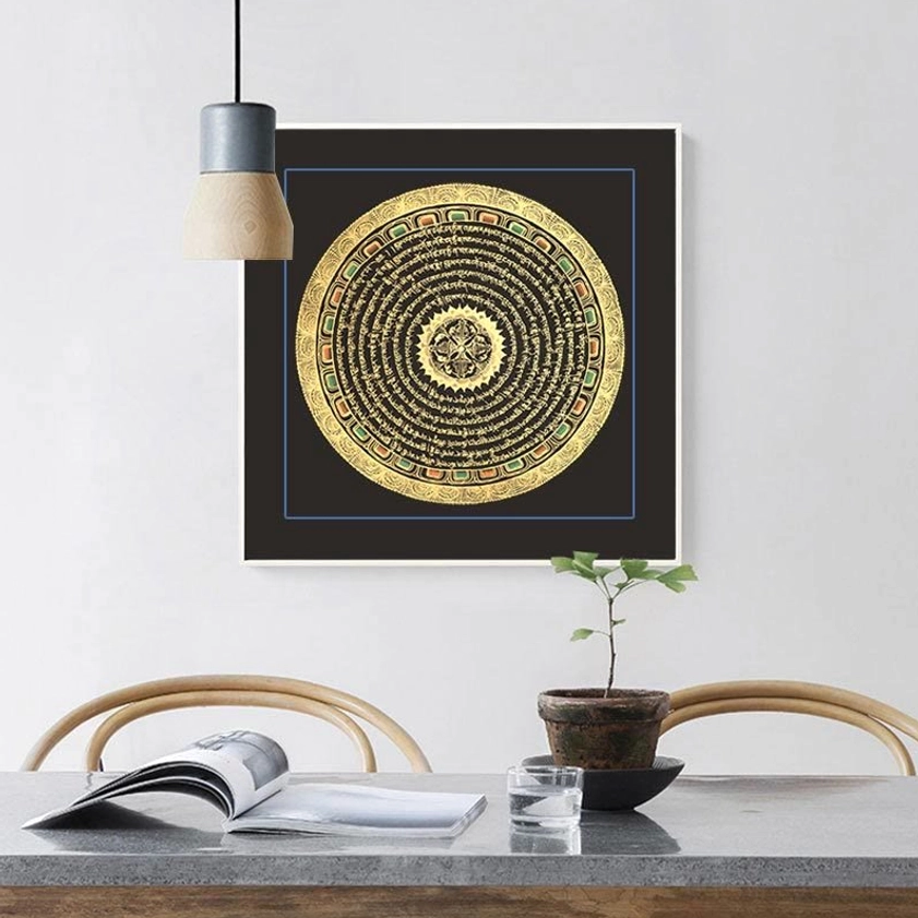 Buddhist thangka scroll with Om Mani Padme Hum mantra displayed at eye-level in modern dining space, featuring black frame with blue trim and gilded mandala artwork
