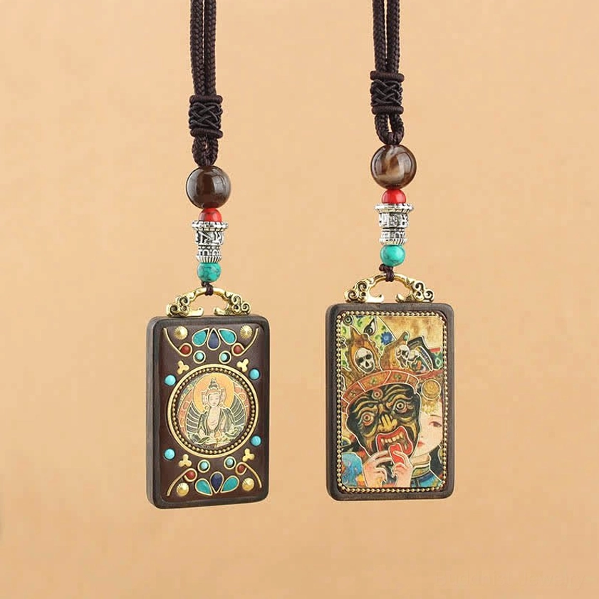 Pair of authentic Buddhist Thangka ebony pendants hanging front view, displaying different deity designs with braided cord and metal hardware