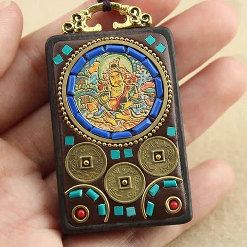 Close-up hand-held view of Buddhist Thangka ebony wood pendant, showing wealth deity pattern with turquoise and red bead inlays and metal hardware