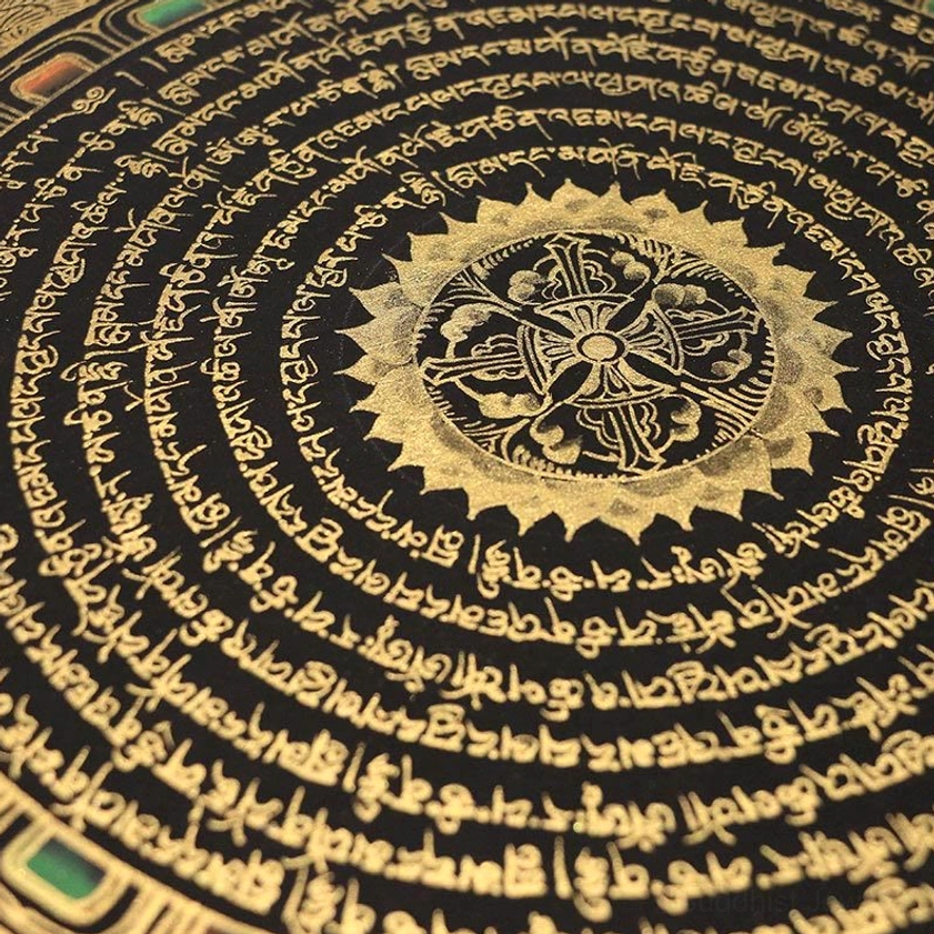 Macro close-up detail of hand-painted Buddhist thangka showing intricate gilded Tibetan script and central dharma wheel mandala motif on black background