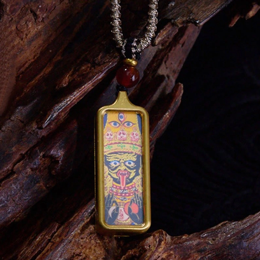 Rectangular Buddhist thangka pendant necklace featuring deity artwork with gold frame, red agate bead and twisted silver cord, close-up detail shot