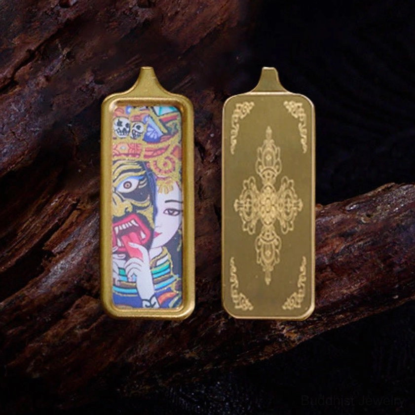 Double-sided Buddhist thangka pendant necklace with gold metal frames and folk deity artwork, flat lay on dark wood backdrop