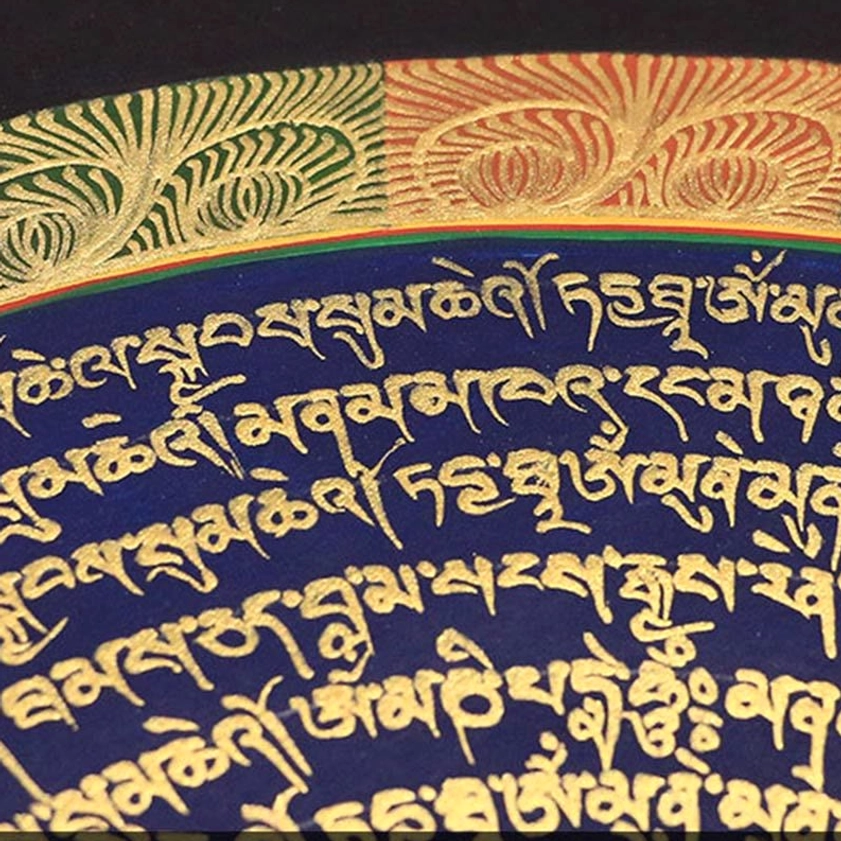 Close-up detail photograph of Buddhist thangka artwork showing delicate gilded Tibetan scripture with ornate floral decorative borders on dark blue background