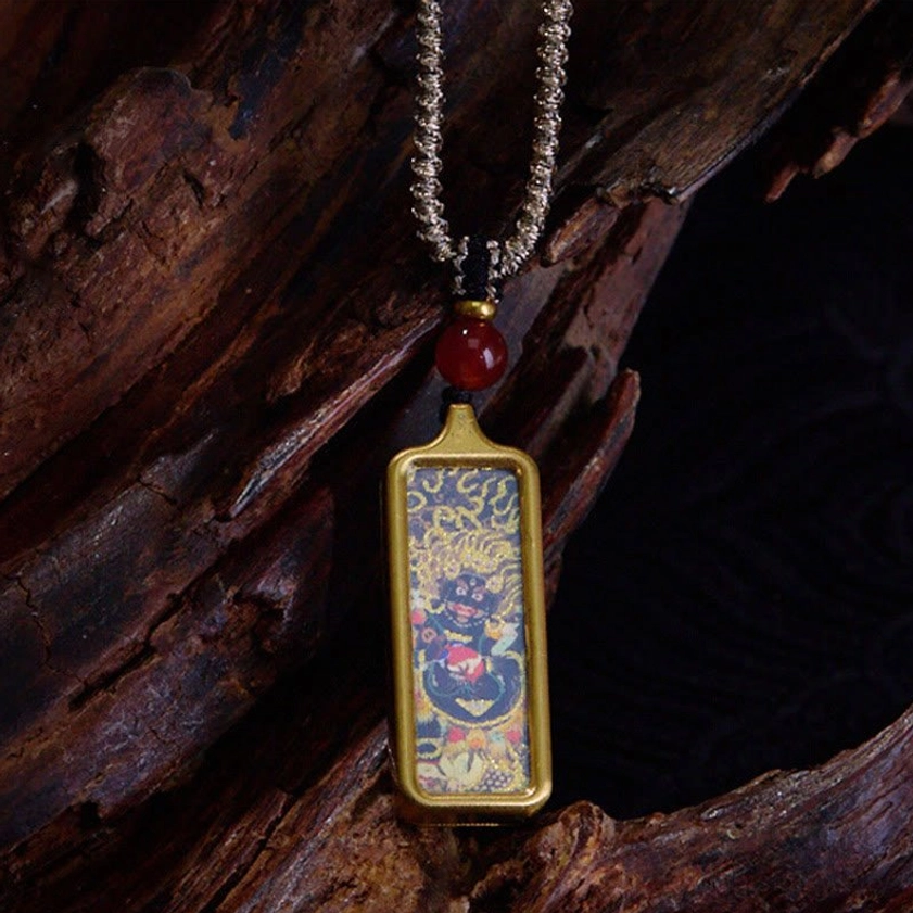 Wrathful Buddhist deity thangka pendant necklace with gold frame, red agate bead, twisted silver cord on dark wood backdrop