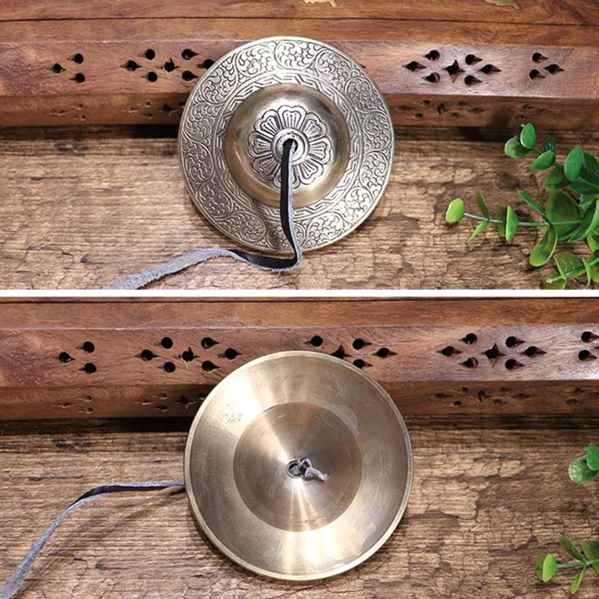 Single Buddhist tingsha bell with embossed floral center and leather hanging strap, artistic wooden backdrop display