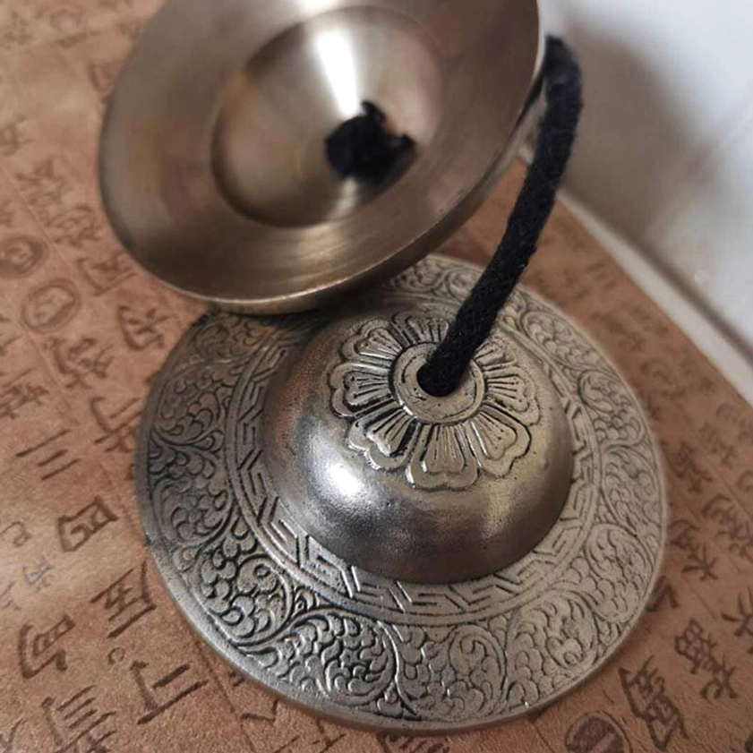Close-up detail of Buddhist tingsha bell showing embossed floral base, polished inner rim and black leather strap connection