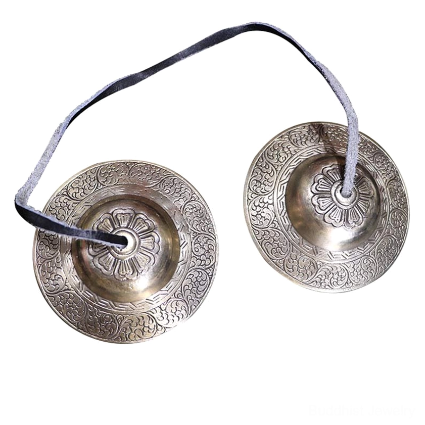 Pair of handcrafted Buddhist tingsha cymbals with detailed floral embossing and individual leather straps on light wooden table