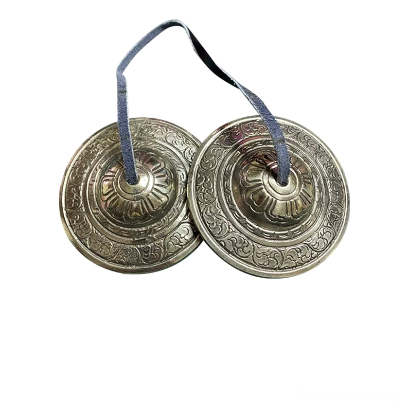 Pair of Buddhist tingsha meditation bells with circular embossed patterns and matching leather hanging cords on dark wooden surface