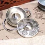 Buddhist tingsha bell pair with sacred mantra engravings on calligraphy cloth, white copper cymbals connected by leather cord