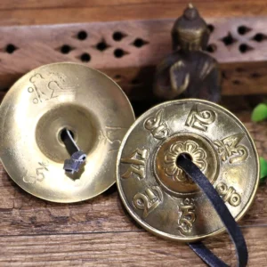 Buddhist tingsha brass cymbals with engraved mantras and leather strap on wooden meditation table