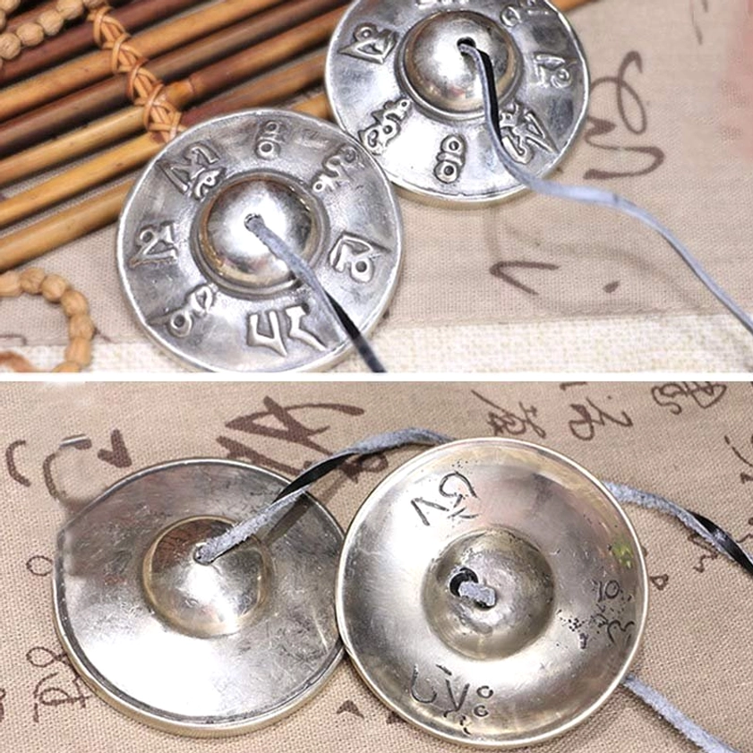 Matched pair of buddhist tingsha bells with mantra engravings on bamboo mat, connected by leather cord, oblique angle