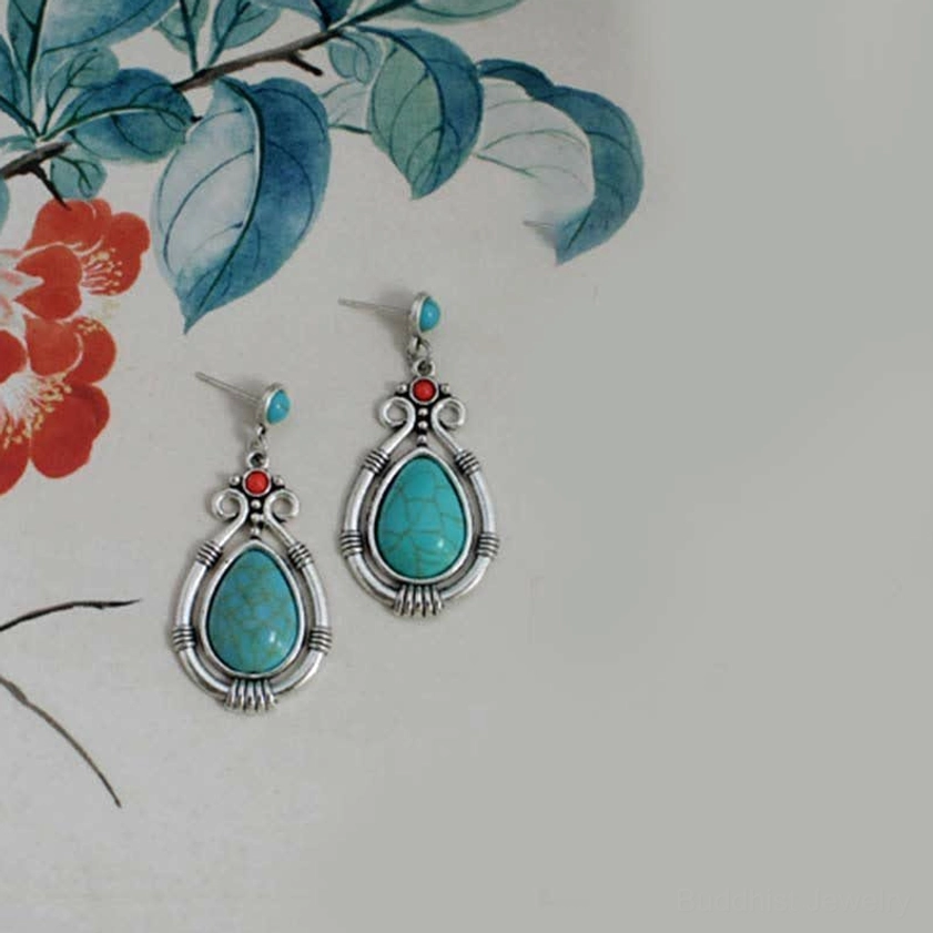 Ethnic turquoise drop earrings displayed on decorative floral art paper background