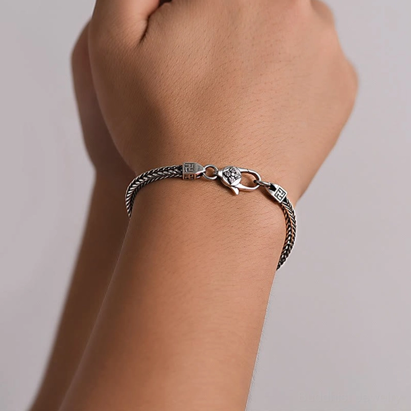 Close-up detail of double vajra Buddhist bracelet on wrist showing chain texture and sacred symbol precision