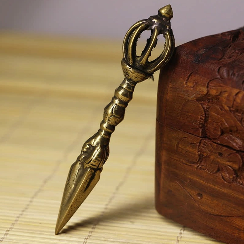 Authentic Buddhist vajra ritual tool with intricate carved details and aged bronze finish, placed on traditional bamboo mat with wooden box