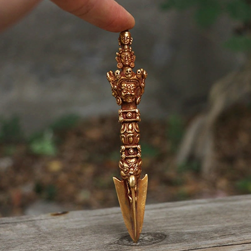 Top-down overhead view of handmade Vajra Dorje held in fingertip, showing multi-faceted carved handle and sharp ritual blade tip