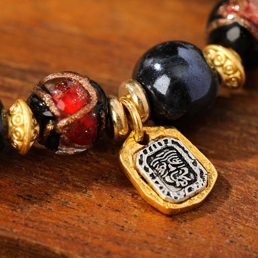 Extreme close-up of Buddhist prosperity bracelet showing red Liuli glass bead and black bead with engraved gold-plated pendant