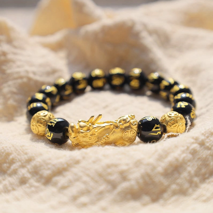 Complete circular obsidian PiXiu bracelet displaying gold charm and alternating black and gold bead pattern on beige fabric