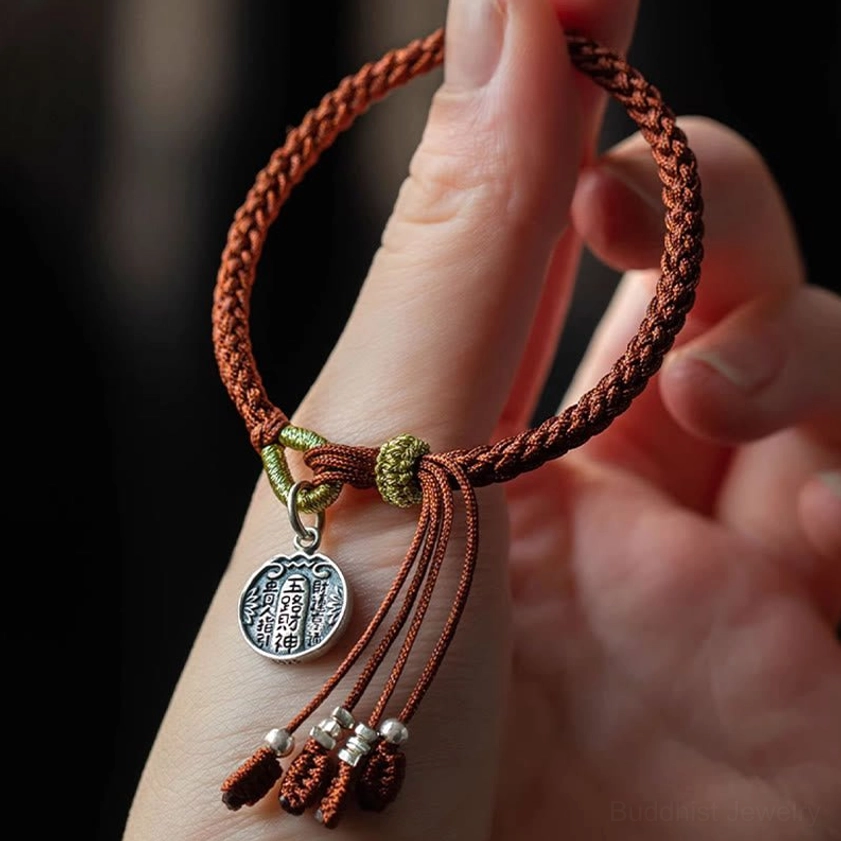 Sterling silver prosperity bracelet with Five Directions Wealth Gods pendant held in hand showing red tassel beads