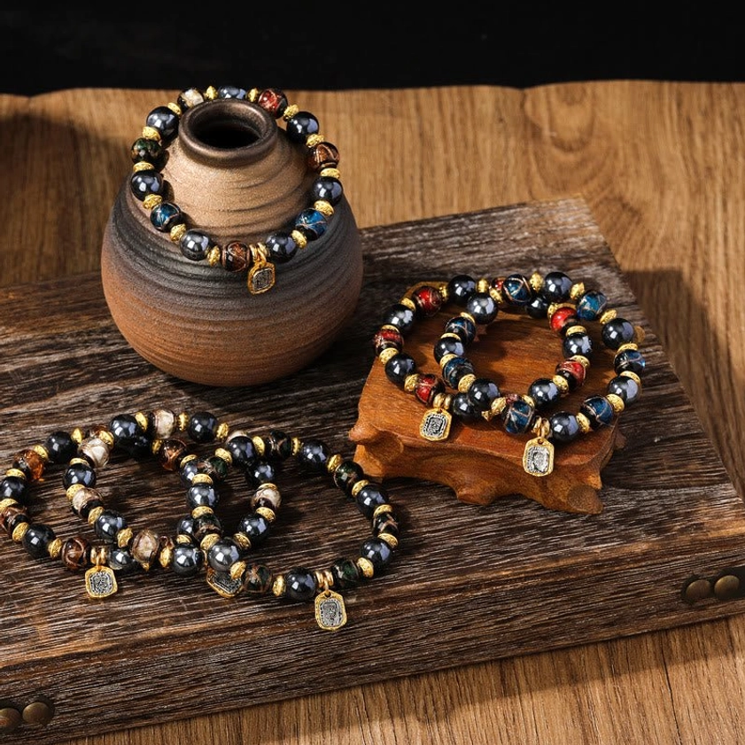 Buddhist prosperity bracelets flat lay featuring dark blue Liuli glass beads with gold spacers and engraved metal pendants on wooden surface