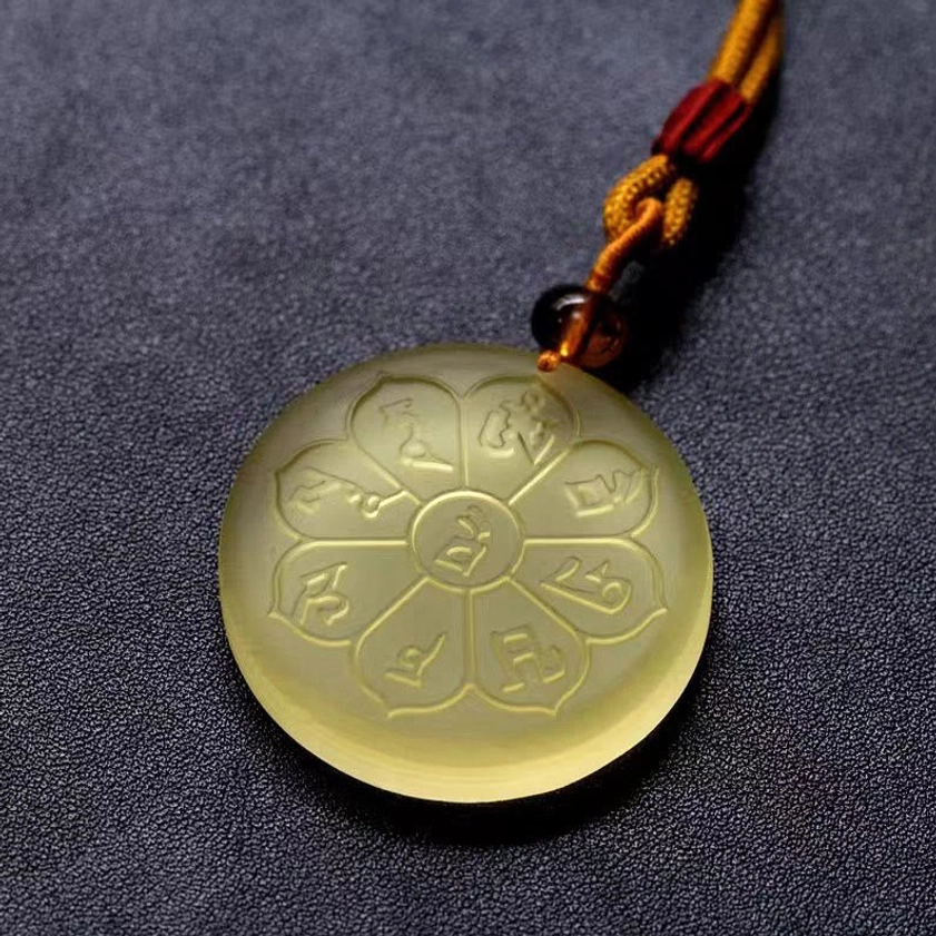 Low angle view of light yellow Liuli crystal eight-petal Buddhist pendant showing full engraved design and polished surface