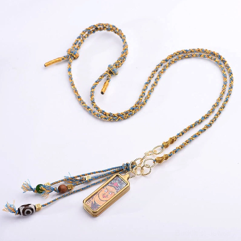 Thangka pendant necklace with braided cord, tassel beads, and rectangular metal frame on pure white background