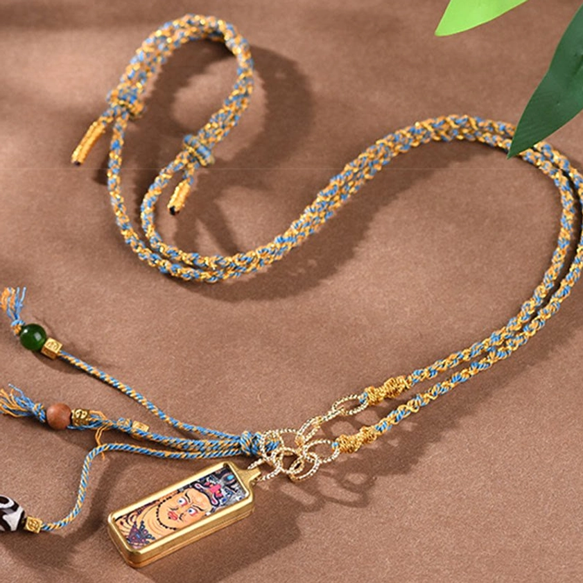 Two matching thangka pendant necklaces with green-yellow woven rope and bead accents on natural leaf background