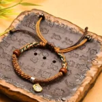 Handmade Buddhist wealth protection bracelet with braided cord and wooden beads displayed on carved stone tray, adjustable drawstring design