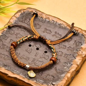 Handmade Buddhist wealth protection bracelet with braided cord and wooden beads displayed on carved stone tray, adjustable drawstring design