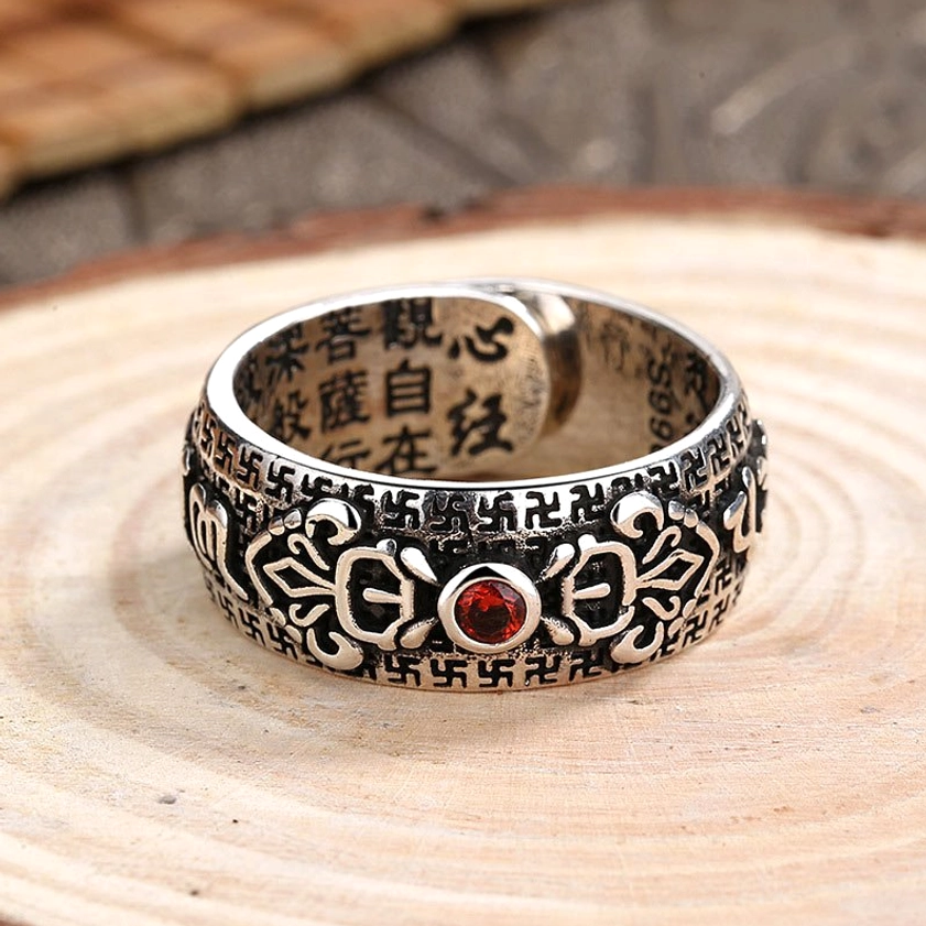 Buddhist prosperity ring front-facing view displaying dual carved Buddhist motifs, Heart Sutra engravings, and polished ruby center gem