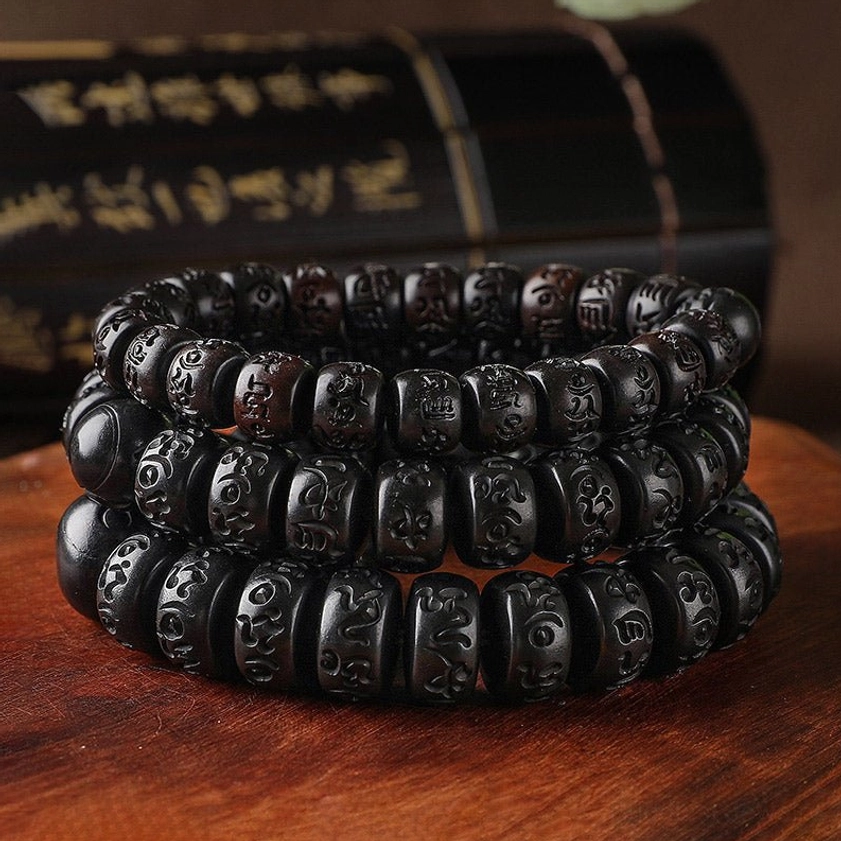 Stacked Buddhist wooden prayer bead bracelets with deep black engraved mantra beads and drum-shaped design on wooden surface