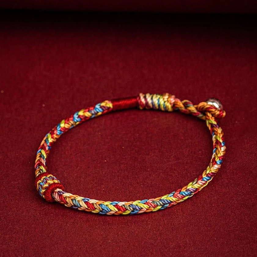 Full view of handmade lucky rope bracelet with braided multicolored strands and metal fastener bead on wine-red background