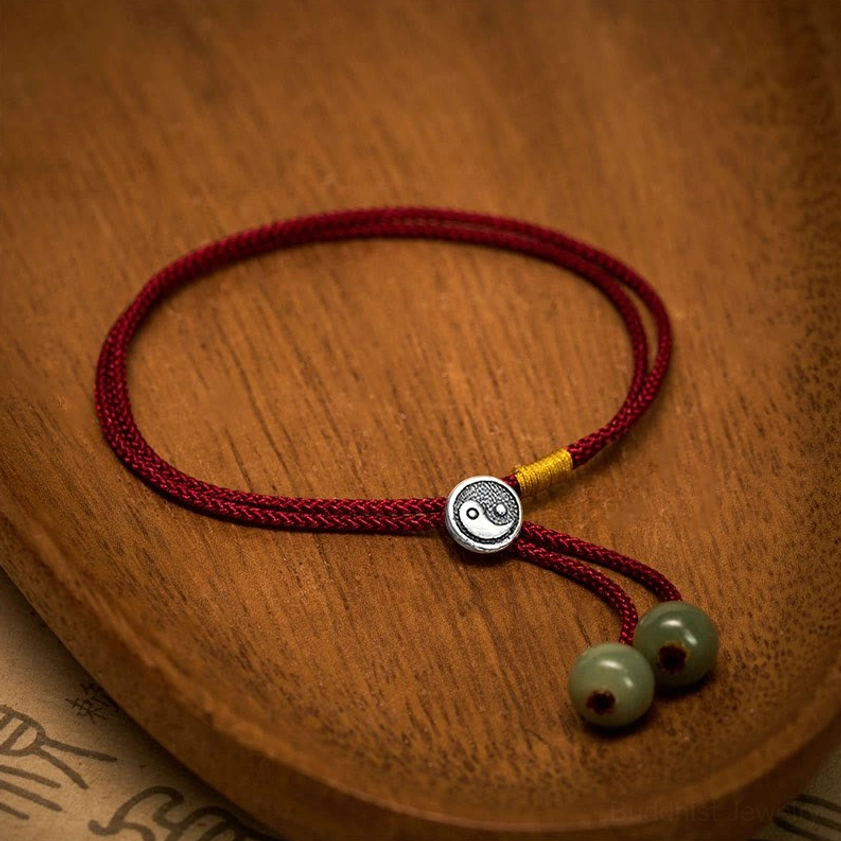 Yin Yang red string bracelet featuring adjustable sliding knot tassel, 925 silver charm, and handwoven braided cord on traditional wooden tray