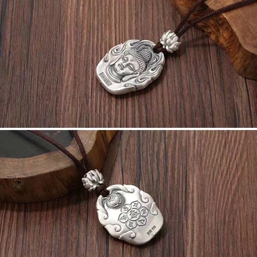 Natal Buddha silver pendant necklace side top-down view on wooden desk, showing matte silver finish, brown hanging cord, and lotus buckle detail