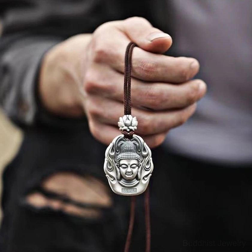 Buddha head pendant necklace worn in hand, showing matte silver finish with lotus buckle and dark brown cord in daily casual first-person view