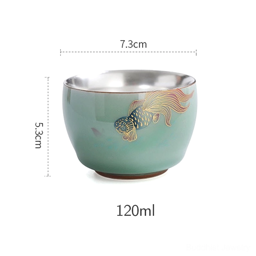 Frontal eye-level view of celadon tea cup with blue butterfly print and silver-lined interior design detail