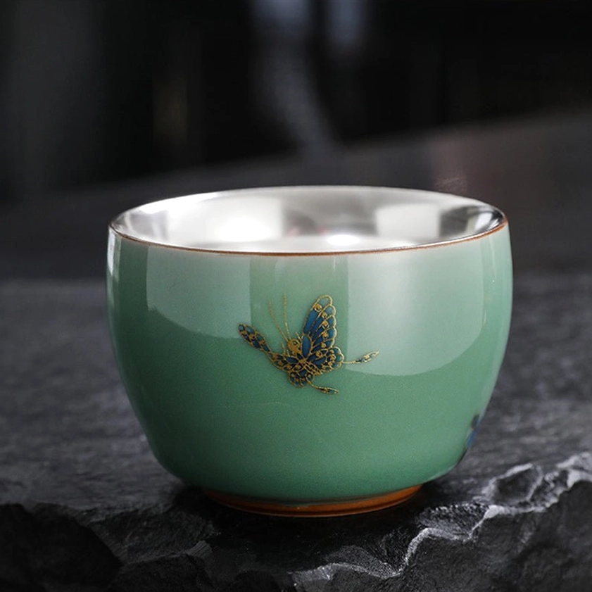 Blue butterfly design celadon tea cup with silver interior, front view of hand-painted Buddhist spiritual motif