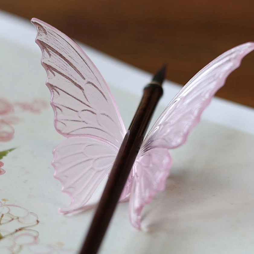 Pink glass butterfly decoration holding writing brush on art supply desk
