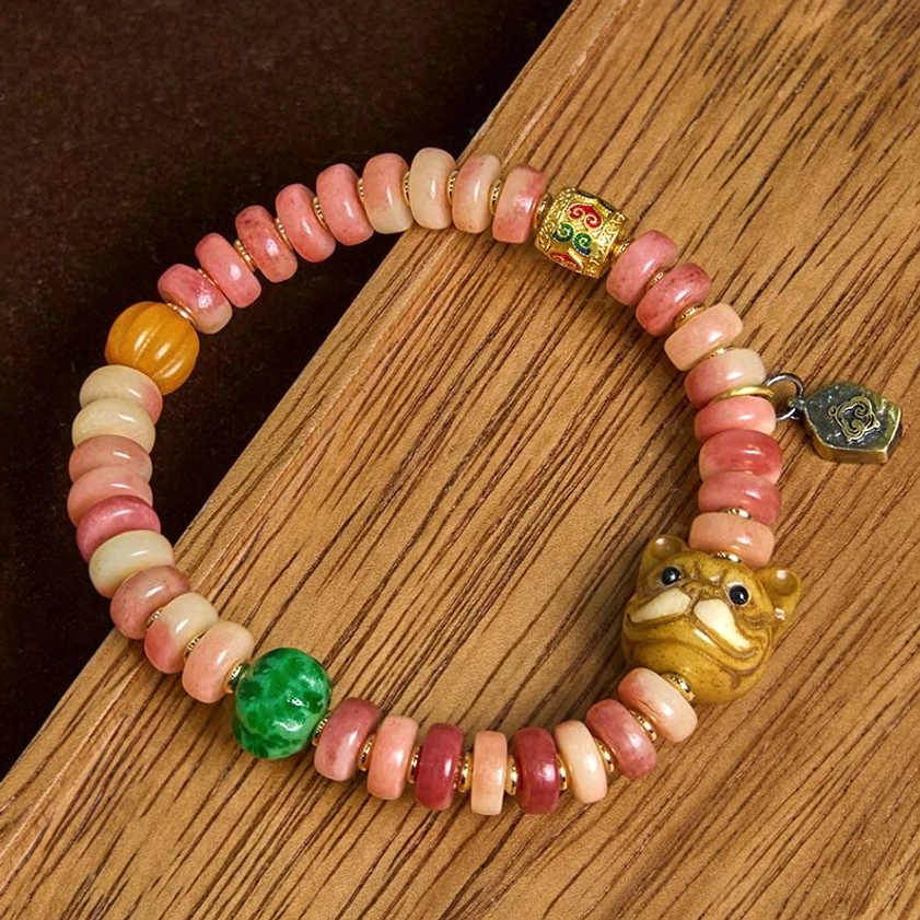 Artisan-made camel bone beaded bracelet with warm pink gradient beads, carved pug head charm, green stone bead - overhead perspective