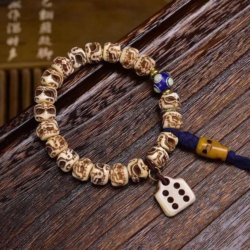 Camel bone dice-style tassel bracelet with blue enamel bead and dark blue tassel on wooden surface