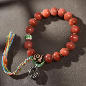 Handcrafted camel bone and dzi bead Buddhist bracelet with colorful tassel charm, featuring protective copper accents and red agate beads for spiritual luck and good fortune