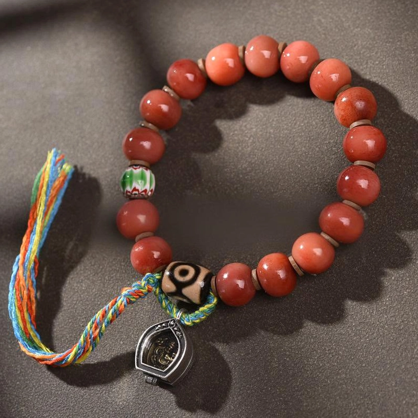 Handcrafted camel bone and dzi bead Buddhist bracelet with colorful tassel charm, featuring protective copper accents and red agate beads for spiritual luck and good fortune