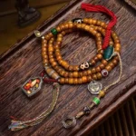 108 bead camel bone Buddhist prayer mala flat lay featuring natural bone beads, dzi stones, agate accents, metal charms, and woven tassel on vintage wooden surface