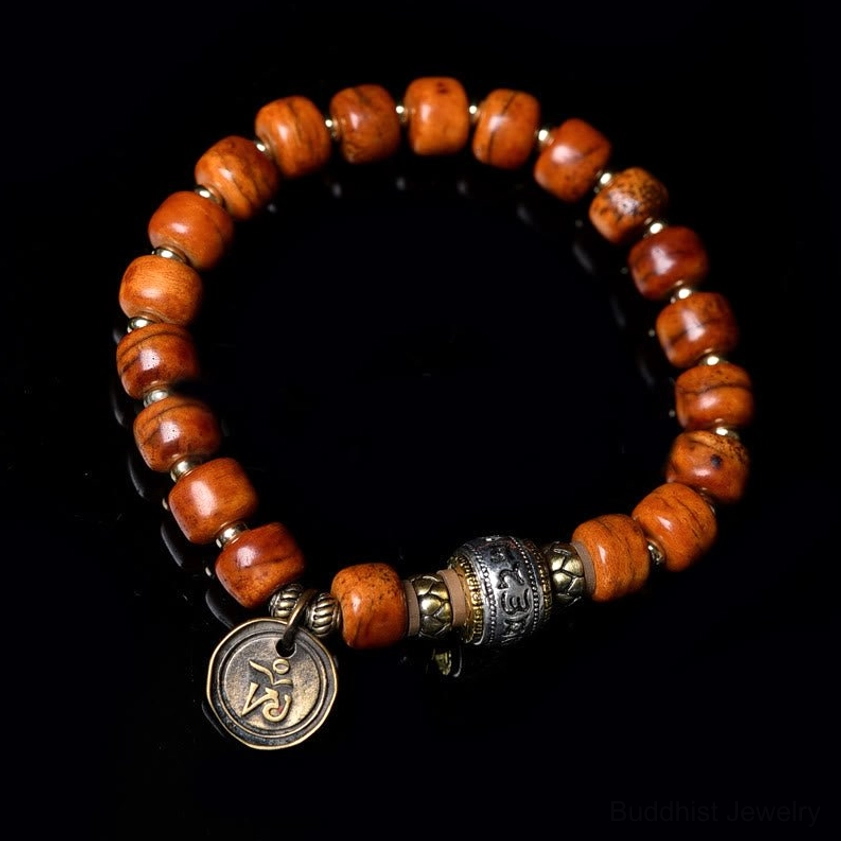 Overhead flat lay of authentic camel bone OM bracelet with warm brown barrel beads, mixed metal spacers, and engraved round charm on dark background