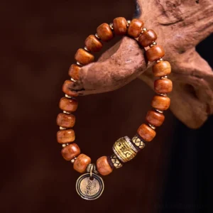 Camel bone OM mantra bracelet with engraved metal charm pendant hanging on wooden prop, showing warm brown barrel beads and decorative metal spacers
