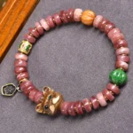 Natural camel bone pug charm beaded bracelet with gradient pink disc beads, green stone, and metal tag pendant - flat lay top view