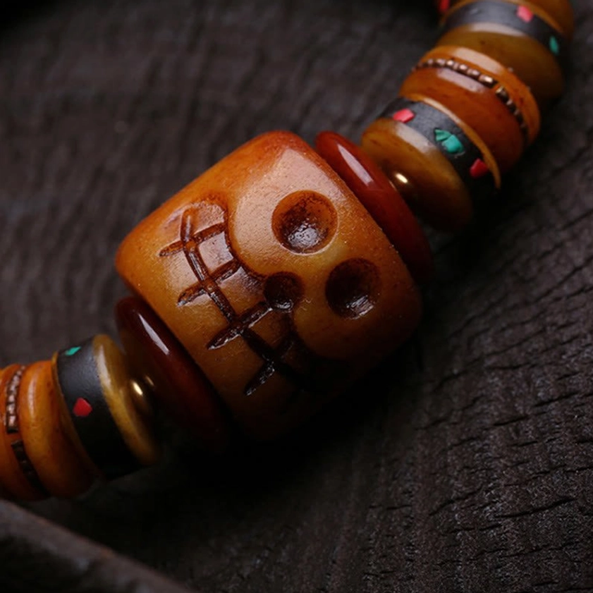 Extreme close-up of carved bone skull bead with cross details and colored inlaid spacers, Buddhist bracelet craftsmanship
