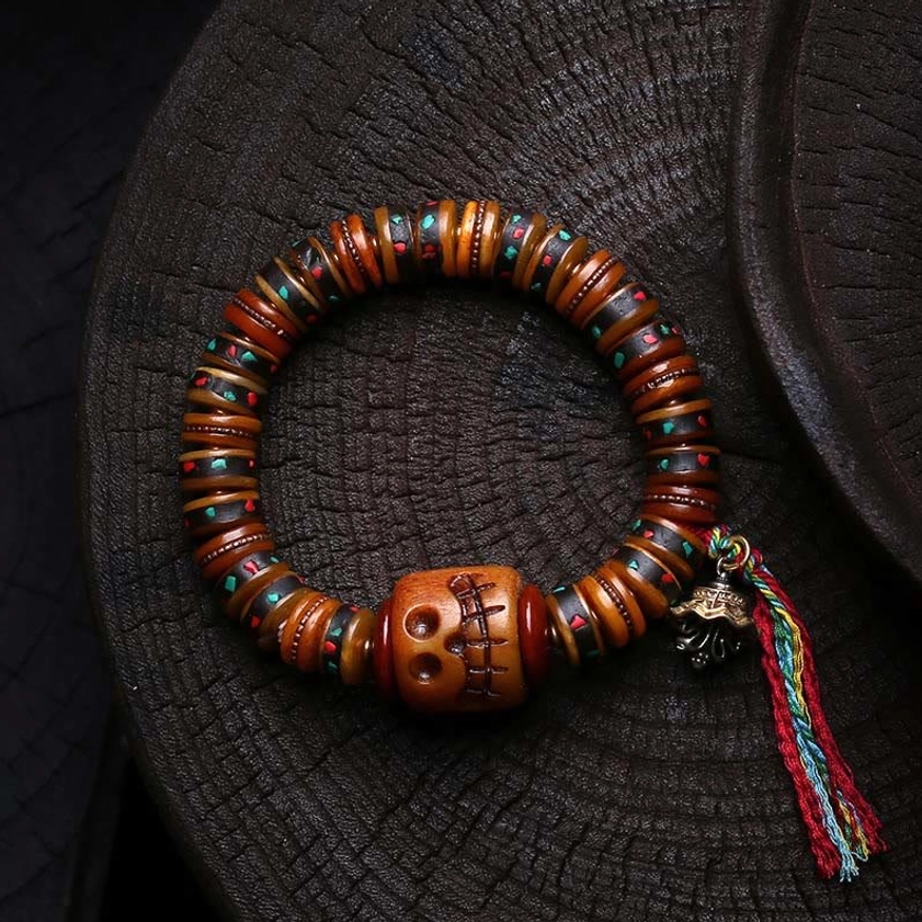 Bone bead bracelet with hand-carved skull bead and colorful tassel accent, flat lay on dark wood surface